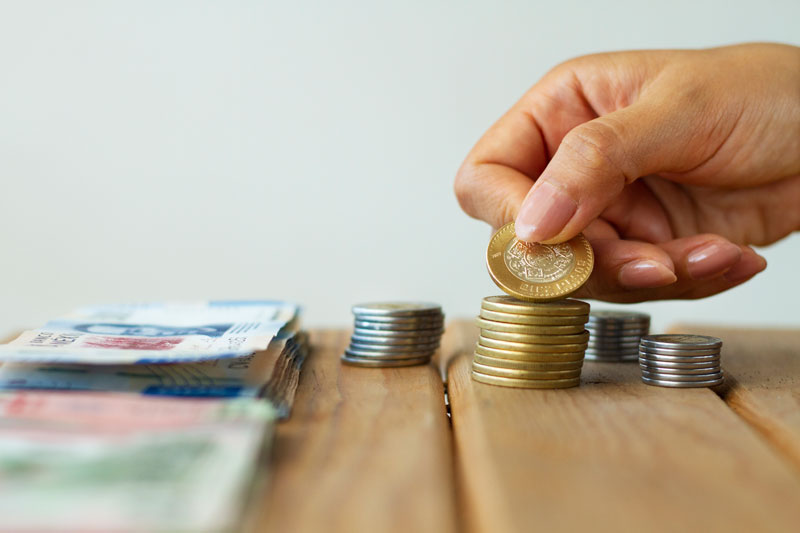 Se muestra en la imagen billetes de dinero y pequeñas montañas de monedas sobre una mesa.